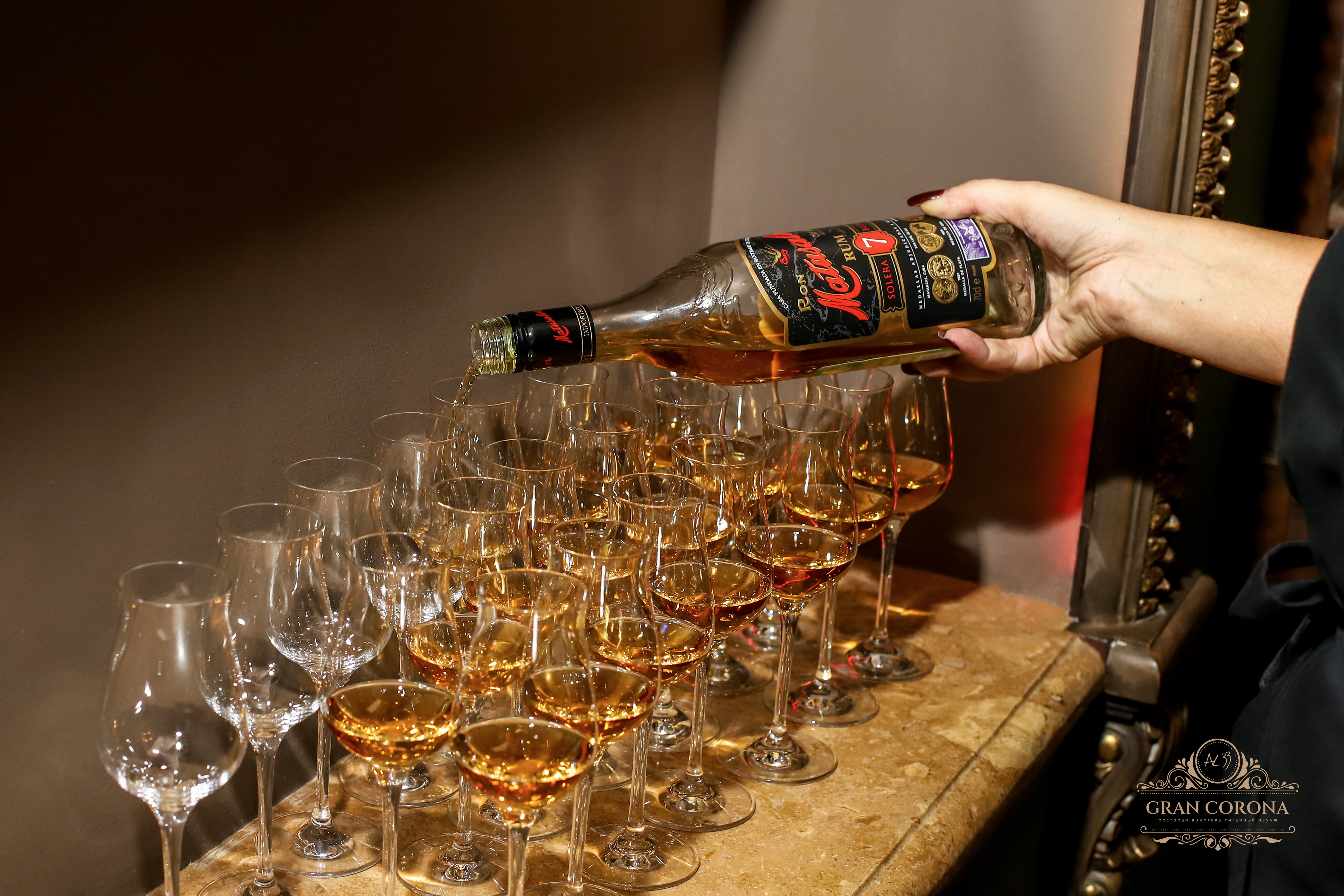 Официант разливает гостям сигарного клуба AL33 Gran Corona доминиканский ром Matusalem по бокалам