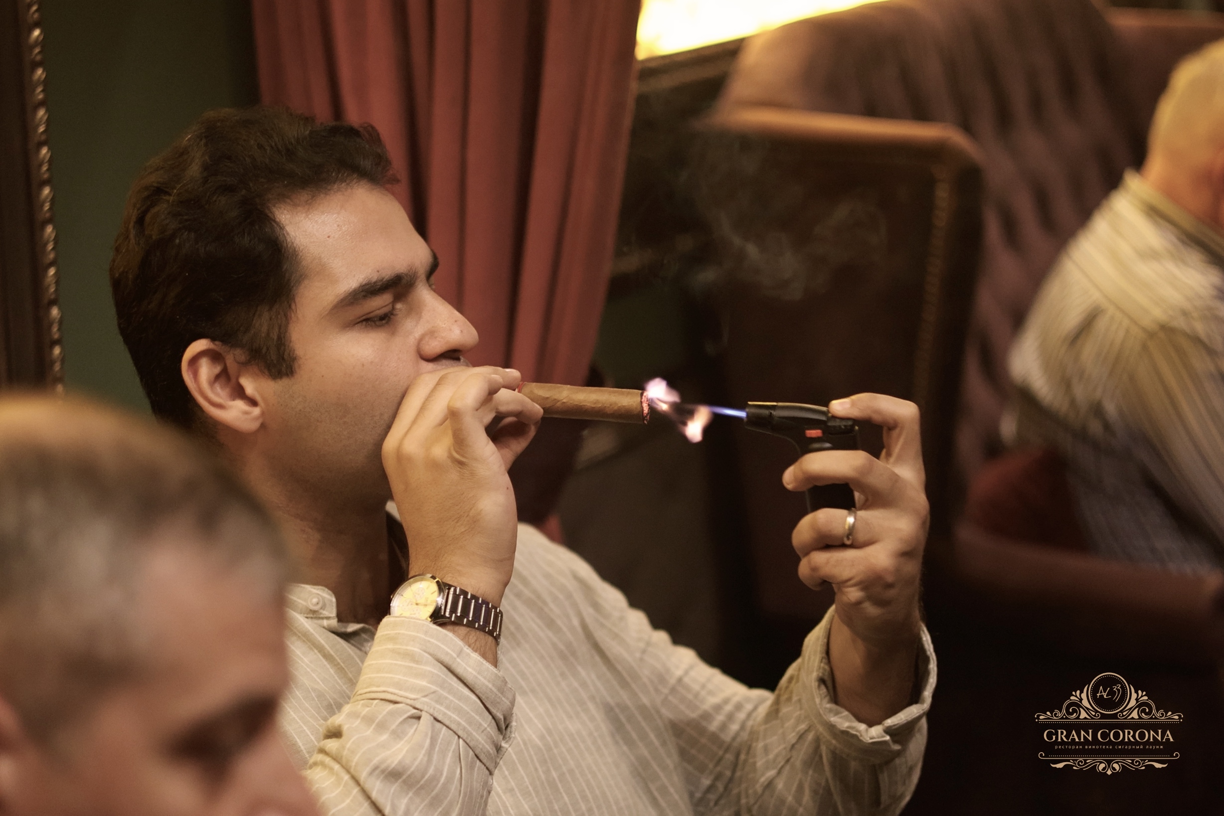 Гость сигарного клуба в Москве поджигает сигару Partagas