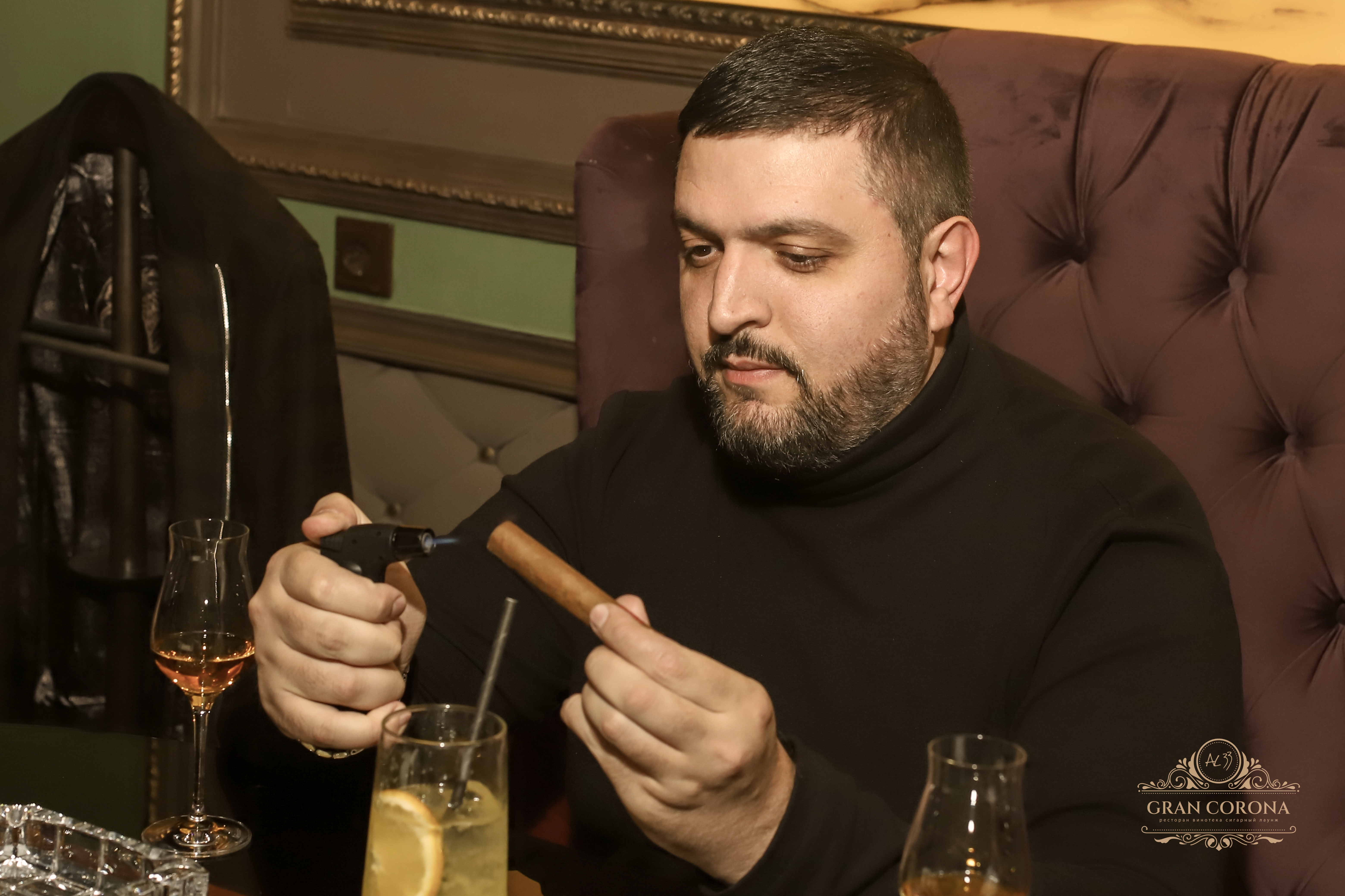 Гость сигарного клуба поджигает сигару зажигалкой блейзером